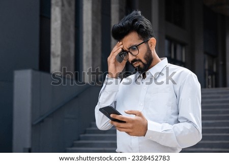 Young hispanic businessman outside office building, man in shirt reading sad bad news online using app on phone, depressed man disappointed unhappy with achievement results. Royalty-Free Stock Photo #2328452783