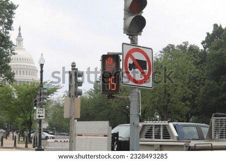 A photo of a crosswalk countdown, a traffic light  and a traffic sign with the Capitol in the horizon in Washington DC.