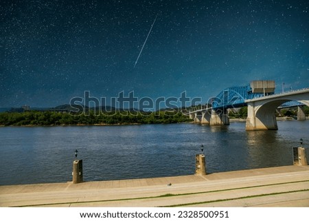 a gorgeous summer landscape on the Tennessee River with the Chief John Ross Bridge over the water and lush green trees and grass along the banks with a beautiful night sky in Chattanooga Tennessee Royalty-Free Stock Photo #2328500951