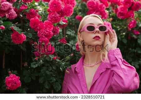 Fashionable woman wearing trendy pink retro style sunglasses, beaded necklace, linen summer shirt, posing in rose garden, among flowers. Copy, empty space for text

 Royalty-Free Stock Photo #2328510721