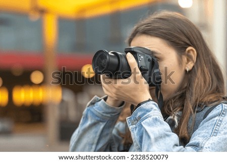 Close up of female photographer with professional camera covering her face taking photo in the city.
