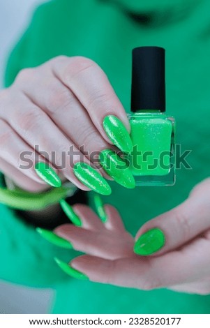 Female hand with long nails and neon green manicure with bottles of nail polish