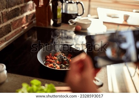Young woman using a smart phone to take a picture of a meal she is cooking