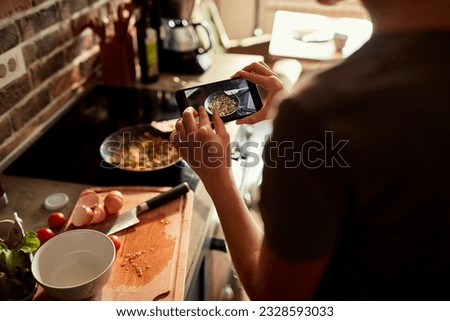 Young woman using a smart phone to take a picture of a meal she is cooking