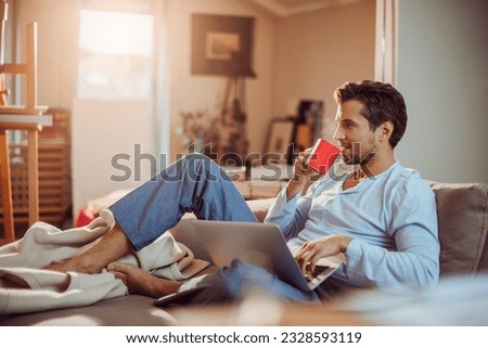 Young man using a laptop in the morning at home and having coffee