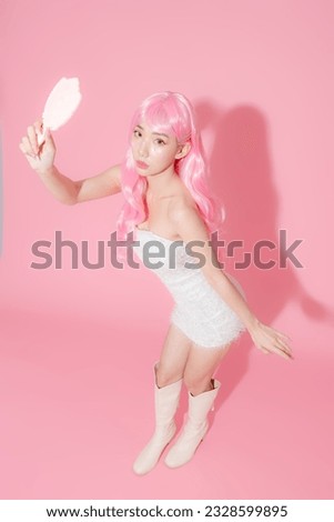 Pretty Asian beautiful woman model long hair with fancy makeup on face and perfect skin holding mirror on isolated pink background. Facial treatment, Cosmetology, plastic surgery.