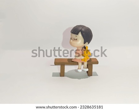 A figurine of a girl sitting on a bench. White background.