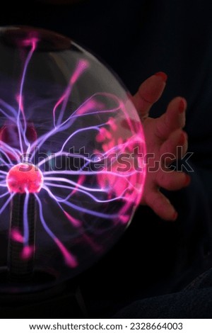plasma ball. Hands holding plasma light ball. Plasma ball light ray science. Finger touching Plasma ball with smooth magenta blue flames. Electromagnetic Fields in a glass globe. Royalty-Free Stock Photo #2328664003