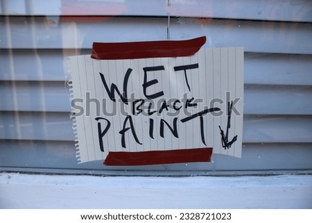 Hand written sign "Wet black paint" with arrow pointing down attached to a window with brown tape