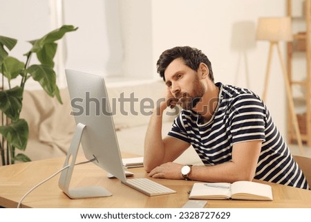 Home workplace. Tired man working with computer at wooden desk in room