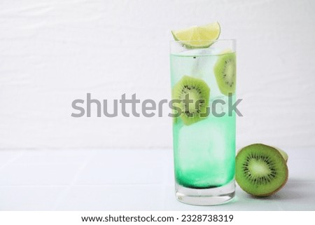 Glass of refreshing drink and cut kiwi on white table. Space for text