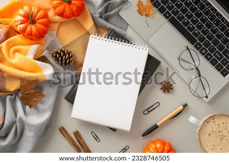 Coziness of working from home with laptop concept. Above view photo of notebook surrounded by blanket, pumpkins, pinecones and spices, office supplies, glasses and laptop on isolated grey background