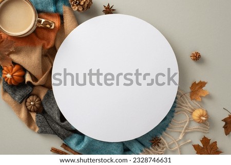 Experience the cozy bliss of autumn at home with this top view photo. Hot coffee, warm blanket, pumpkin candles, maple foliage and spices set the empty circle for text or advert on grey backdrop