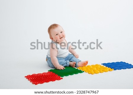 the baby is sitting on a baby foot massage mat on a white background.Exercises for the legs on an orthopedic massage mat. high quality photos