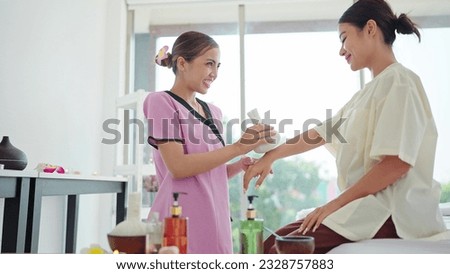Asian woman therapist using spa herbal balls steamed to relieve pain and reduce swelling in wrist of woman client sitting on masseuse bed. Wellness massage and treatment concept Royalty-Free Stock Photo #2328757883