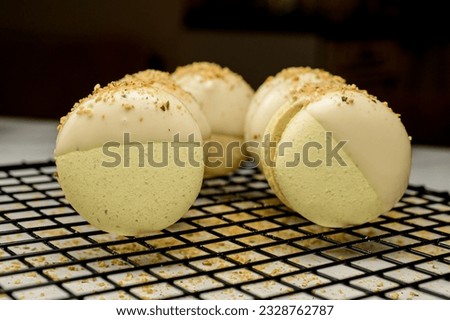 Fresh tasty pistachio macarons with sweet ganache decorated with white chocolate, chopped peanuts and pistachios stacked on cooling rack on blurred background