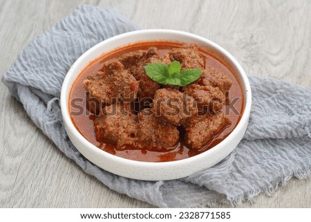beef rendang or rendang daging is a Minangkabau dish made of meat that has been braised in coconut milk seasoned with herb and spice mixture until the meat brown. served on white plate. selected focus