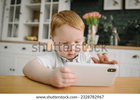 Toddler playing mobile device video game. Child watching cartoons online on phone at home alone. Cute little boy using smartphone, looking at screen. Kid gen Z using parental control app on cell phone