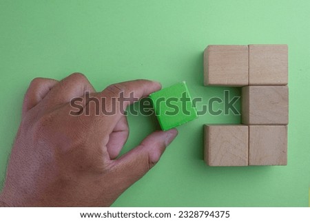 Hand picking Green wooden block among wooden blocks over green background.