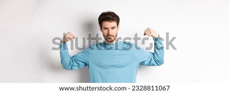 Confident and strong macho man flexing biceps, showing strength in muscles after gym workout, standing over white background. Royalty-Free Stock Photo #2328811067