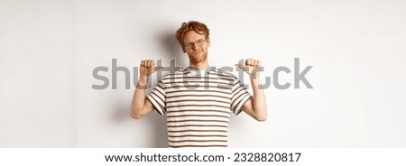 Confident young nerdy guy in glasses with red hair, pointing at himself and looking like professional, white background.