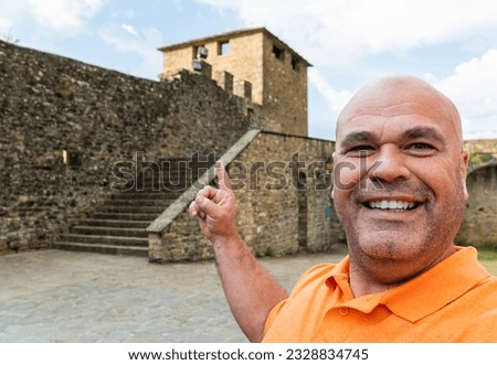 A smiling man takes a photo with a old house in the background