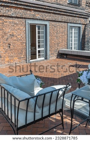 a chic terrace of a country house with wrought iron furniture, vases with flowers and columns on a bright summer sunny day