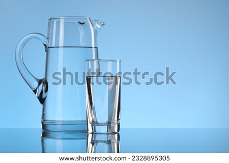 Glass and jug with water on light blue background. Space for text