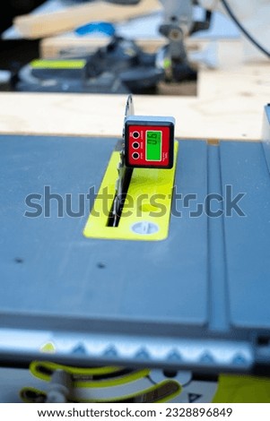 Protractor digital level box inclinometer attaches on steel blade of table saw with mite saw in background of wooden workbench. Bevel gauge for absolute measurements of woodworking, carpentry
