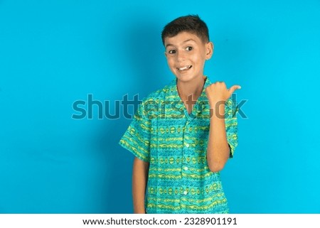 Impressed Little hispanic kid boy wearing green aztec shirt point back empty space