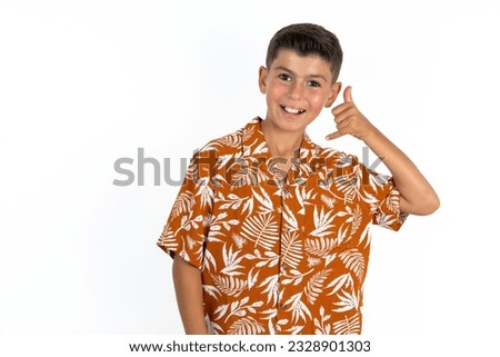 Little hispanic kid boy wearing hawaiian shirt smiling doing phone gesture with hand and fingers like talking on the telephone. Communicating concepts.