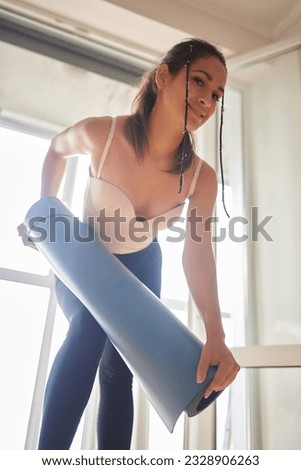 Close-up of an attractive young woman laying out a blue yoga or fitness mat before exercising in the studio. Healthy lifestyle