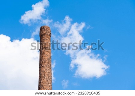 Old ruined brick chimney in front of cloudy blue sky