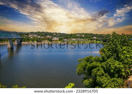 a beautiful summer landscape at the along the Tennessee River at the Walnut Street Bridge with rippling water and lush green tree and plants and powerful clouds at sunset in Chattanooga Tennessee USA Royalty-Free Stock Photo #2328916705
