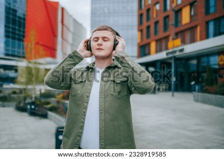 A man wearing a red shirt and headphones, looking at the cityscape while enjoying his music. City Soundtrack Handsome Man with Headphones On Listening to Music Royalty-Free Stock Photo #2328919585