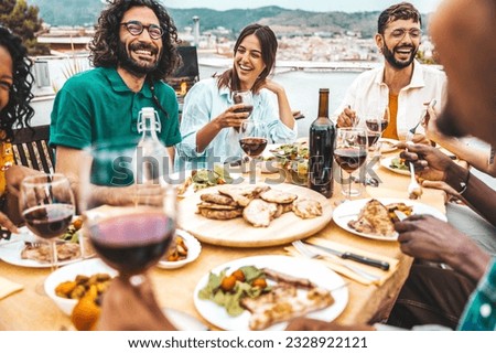 Multiethnic friends having fun at rooftop bbq dinner party - Group of young people diner together sitting at restaurant dining table - Cheerful multiracial teens eating food and drinking wine outside