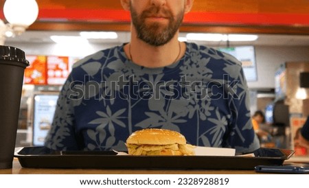 A fresh hamburger on the salver in a dinner and a man ready to eat behind it Royalty-Free Stock Photo #2328928819