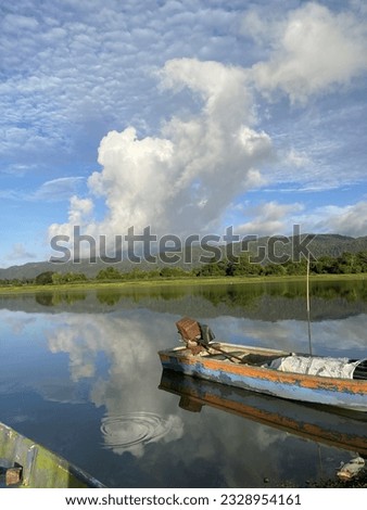 A fishing boat by the lake with no people and beautiful scenery of the clouds and blue sky in the morning