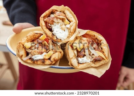 Waiter in red apron presents a plate with three Gyro Pita Shawarma, Souvlaki. Fast food, Greek, Turkish meat food wrap with paper, close up. 
 Royalty-Free Stock Photo #2328970201