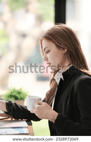Young Asian business woman wearing suit drinking coffee reading a document in the office. Happy smiling female professional working holding a document.