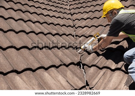 Worker man using silicone sealant adhesive  to fix crack of the old tile roof. Royalty-Free Stock Photo #2328982669