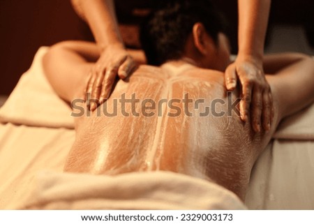 Masseuse hand applying salt scrub on back customer at cosmetology spa centre. Relaxation man customer get service skincare scrubbing massage with masseuse in spa salon. Selective focus. Royalty-Free Stock Photo #2329003173