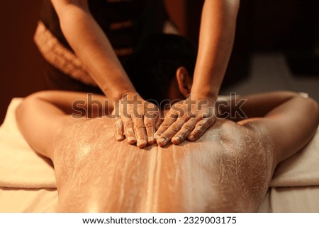 Masseuse hand applying salt scrub on back customer at cosmetology spa centre. Relaxation man customer get service skincare scrubbing massage with masseuse in spa salon. Selective focus. Royalty-Free Stock Photo #2329003175