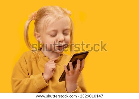 Portrait of child with smartphone. Cheery little girl watching cartoons on mobile phone in isolation on yellow background