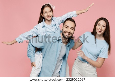 Young fun parents mom dad with child kid daughter teen girl in blue clothes giving piggyback ride to kid, sit on back do fly gesture isolated on plain pastel light pink background Family day concept