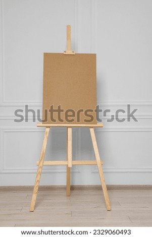 Wooden easel with blank board near white wall indoors