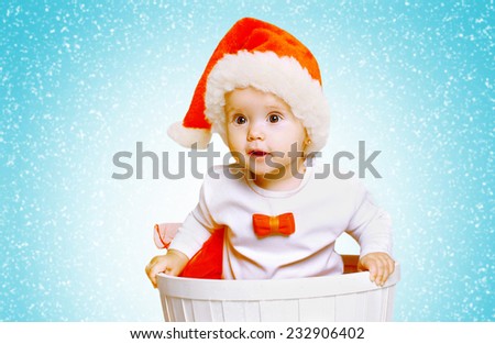 Christmas and people concept - cute curious baby in santa hat and snowflakes