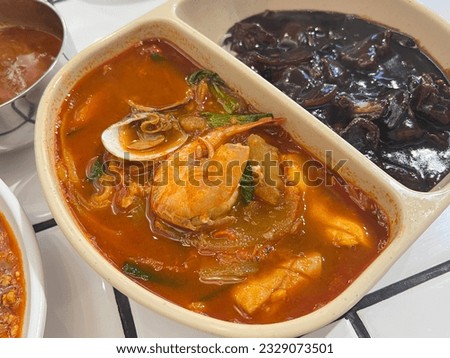 A bowl split between noodles in black sauce, pork and noodles in a spicy seafood soup