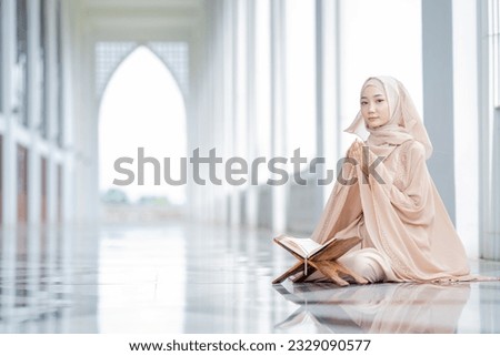 The image of an Asian Muslim woman in the Islamic religion in hijab in white color. reading the Quran, Koran Staying in a beautiful mosque, Arabic word translation: The Holy Al Quran.