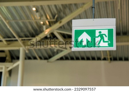 Green emergency exit sign showing the way to escape in an emergency 
fixed to the ceiling at visible height Fire exit in the building
